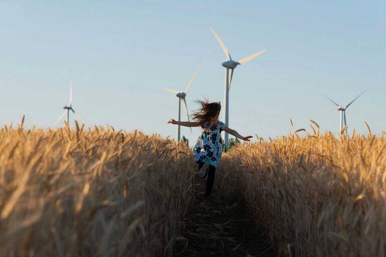 Ein Kind läuft durch ein Kornfeld, während im Hintergrund mehrere Windräder stehen.