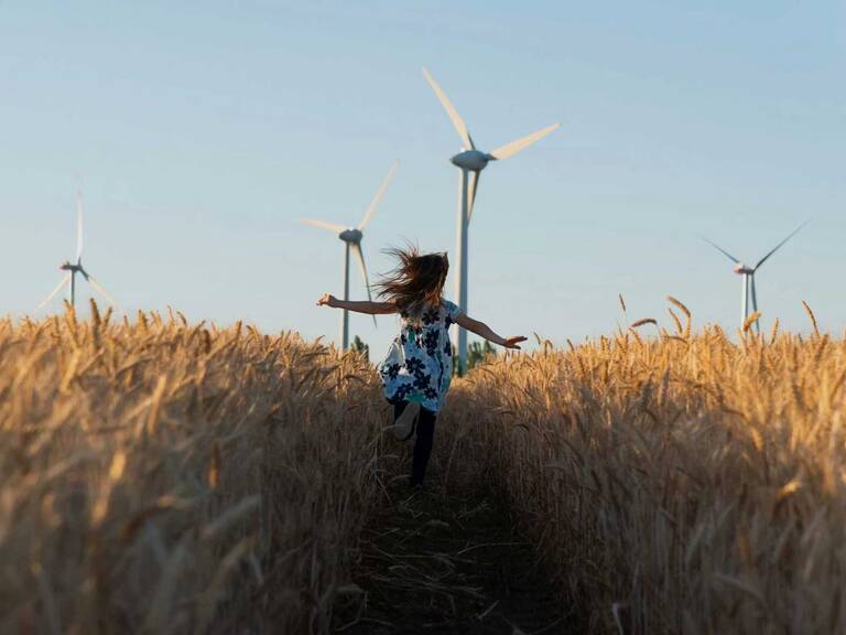 Ein Kind läuft durch ein Kornfeld, während im Hintergrund mehrere Windräder stehen.
