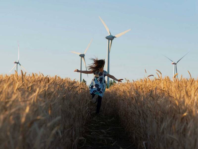 Ein Kind läuft durch ein Kornfeld, während im Hintergrund mehrere Windräder stehen.