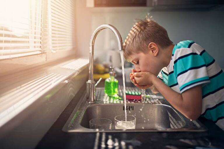 Ein Junge trinkt Wasser direkt aus dem laufenden Wasserhahn in der Küche.