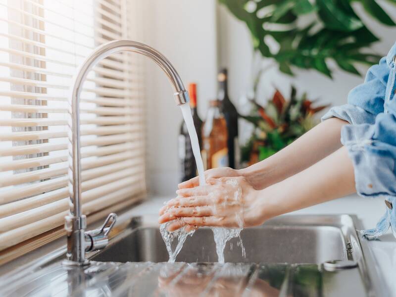 Eine Person wäscht ihre Hände unter einem Wasserstrahl in einem modernen Waschbecken.
