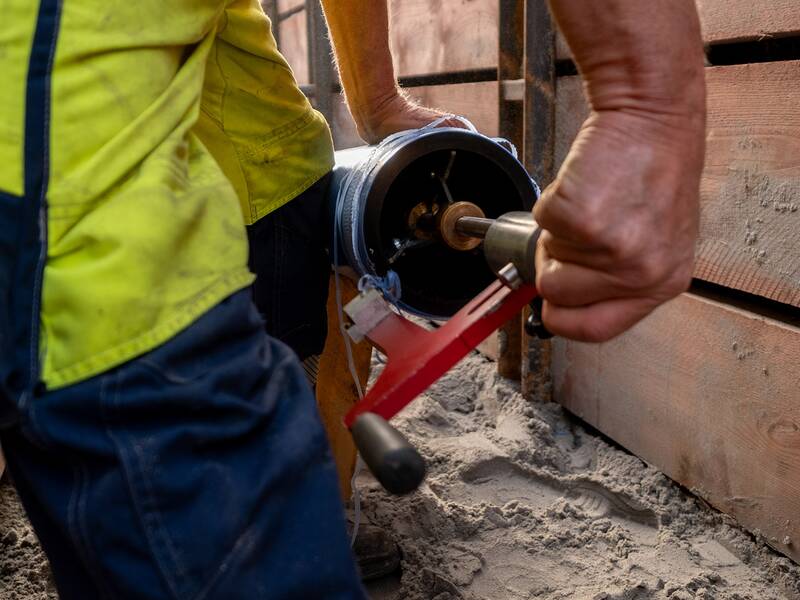 Eine Person in Arbeitskleidung verwendet ein manuelles Werkzeug, um ein Wasserrohr an einer Baustelle zu bearbeiten.