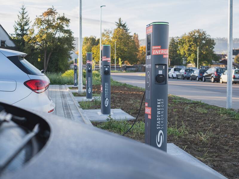 Eine Reihe von Ladestationen für Elektrofahrzeuge steht auf einem Parkplatz, während ein Auto an einer der Stationen parkt.
