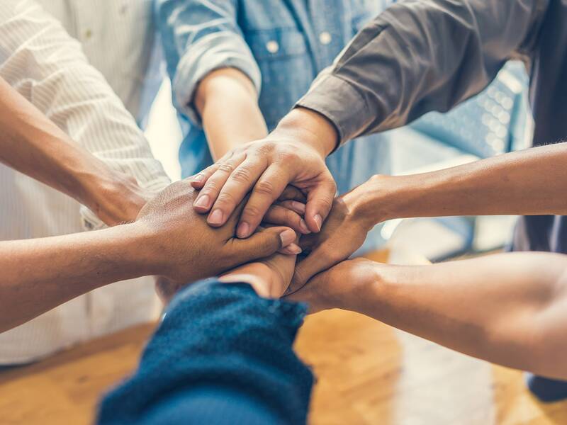 Mehrere Personen legen ihre Hände übereinander, was Zusammenarbeit oder Zusammenhalt symbolisiert.