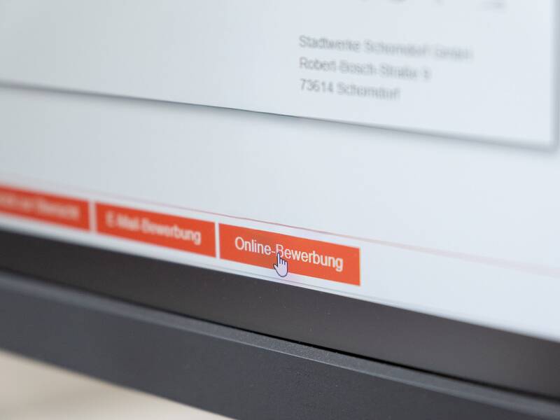Ein Computerbildschirm zeigt eine Webseite mit einem hervorgehobenen orangefarbenen Button, der die Option "Online-Bewerbung" anbietet.