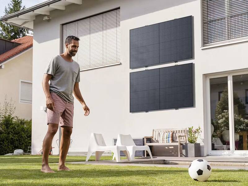 Ein Mann und ein Junge spielen mit einem Fußball im Garten vor einem Haus mit Solarmodulen an der Fassade.